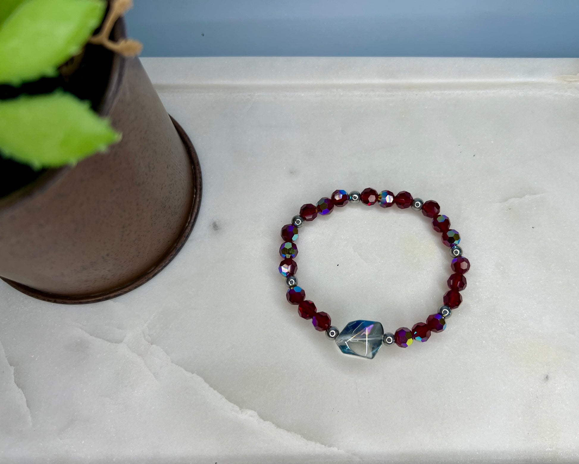 a red beaded bracelet sitting next to a potted plant