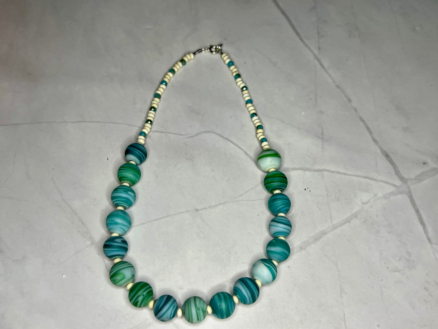 a necklace with green and white beads on a white surface