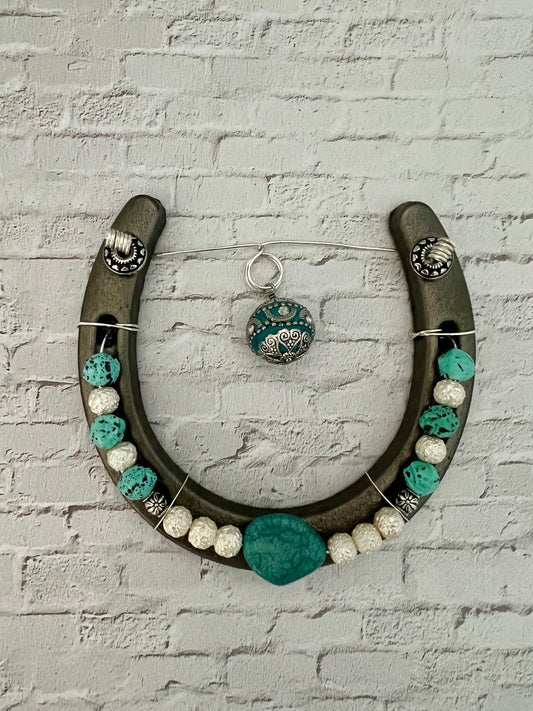 a horseshoe with turquoise and white beads hanging on a brick wall