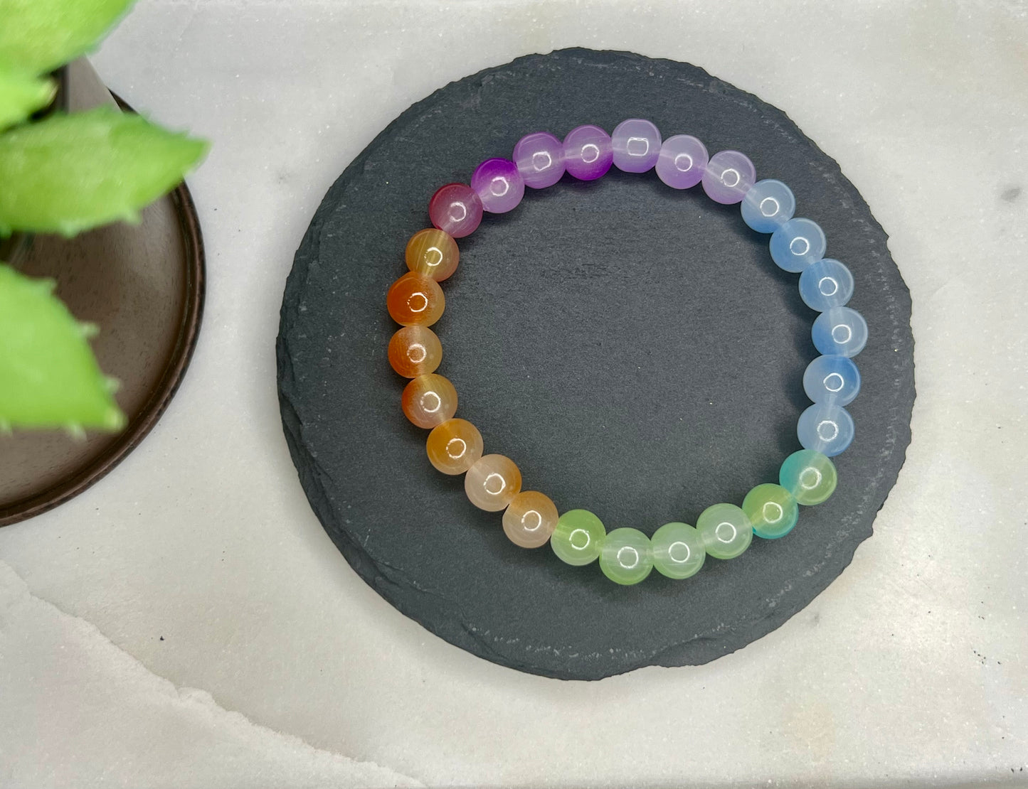 a bracelet made of multicolored beads sits next to a potted plant