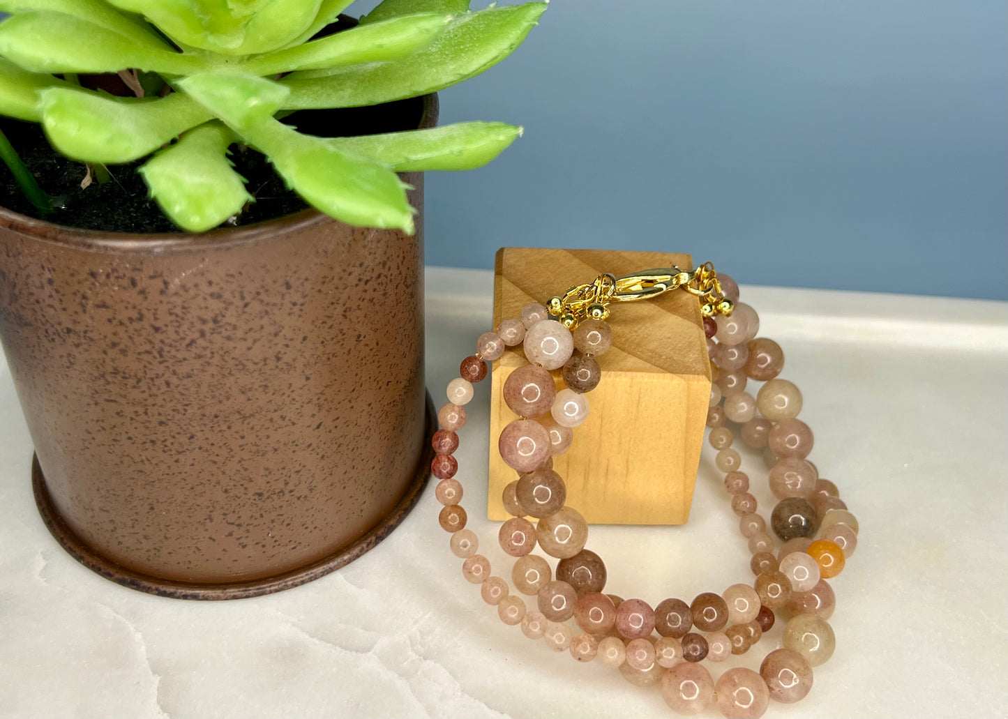 a bracelet with beads and a wooden block on a table next to a potted