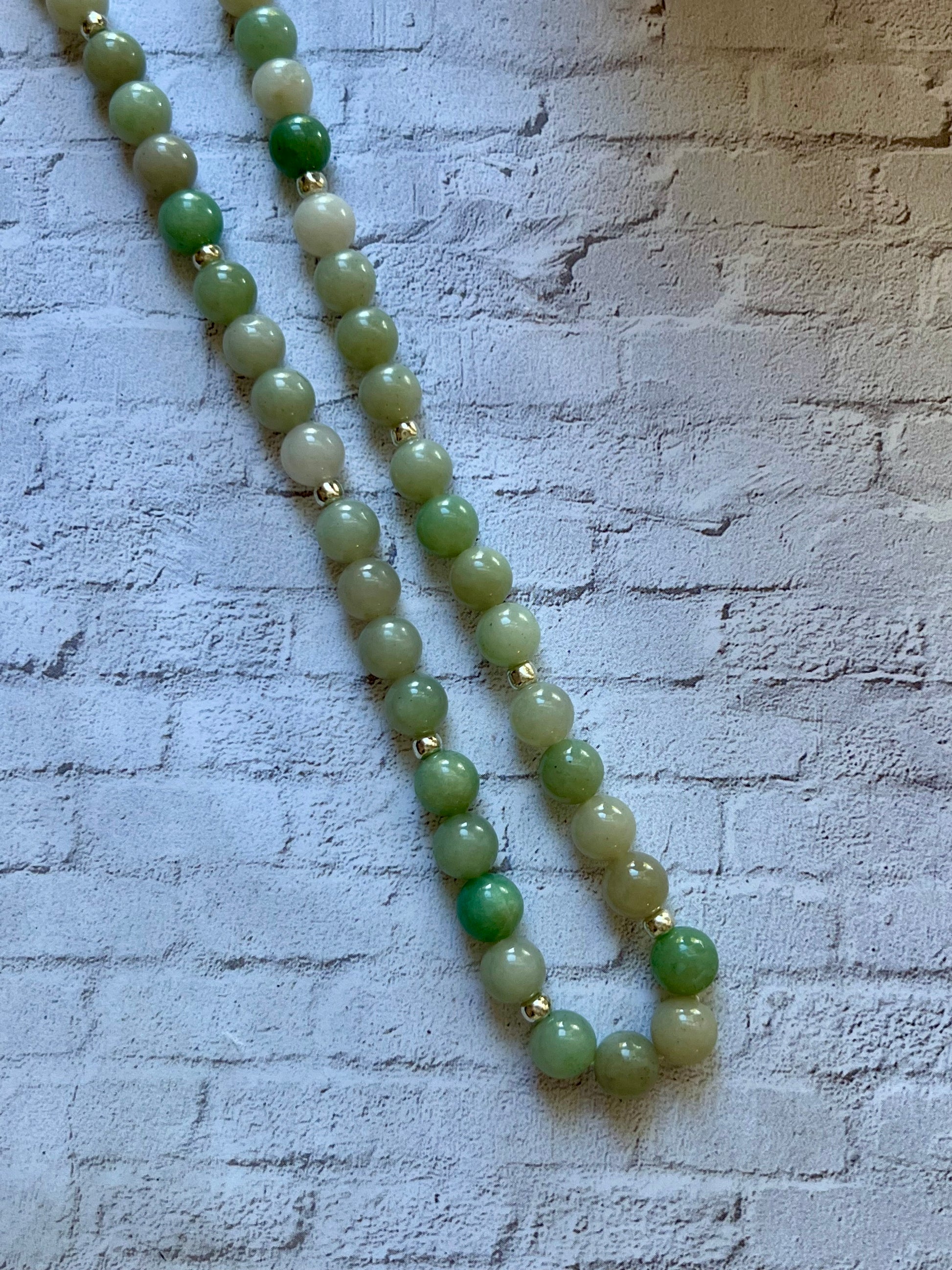 a long green beaded necklace on a white brick wall