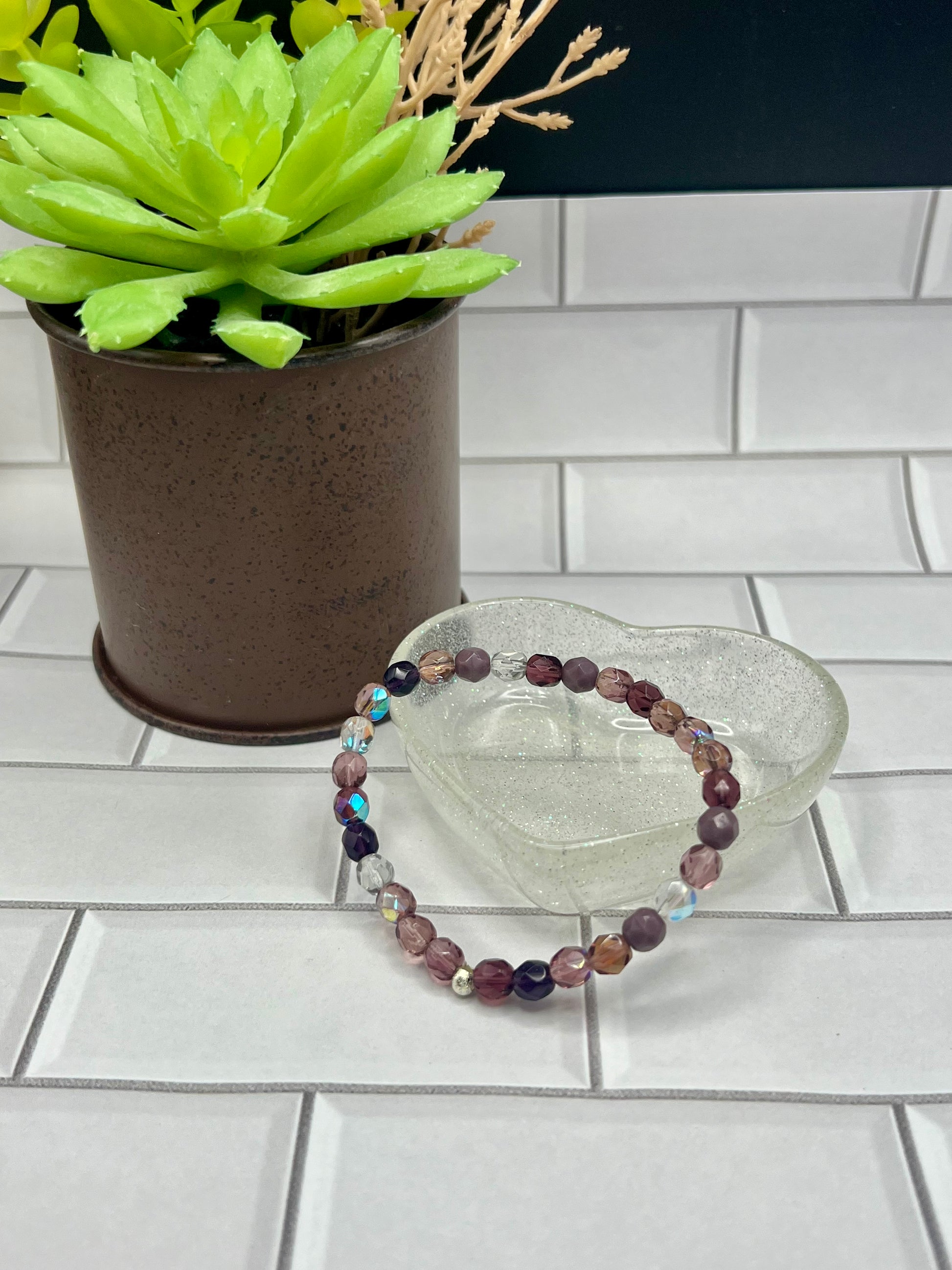 a glass bowl with a beaded bracelet next to a potted plant