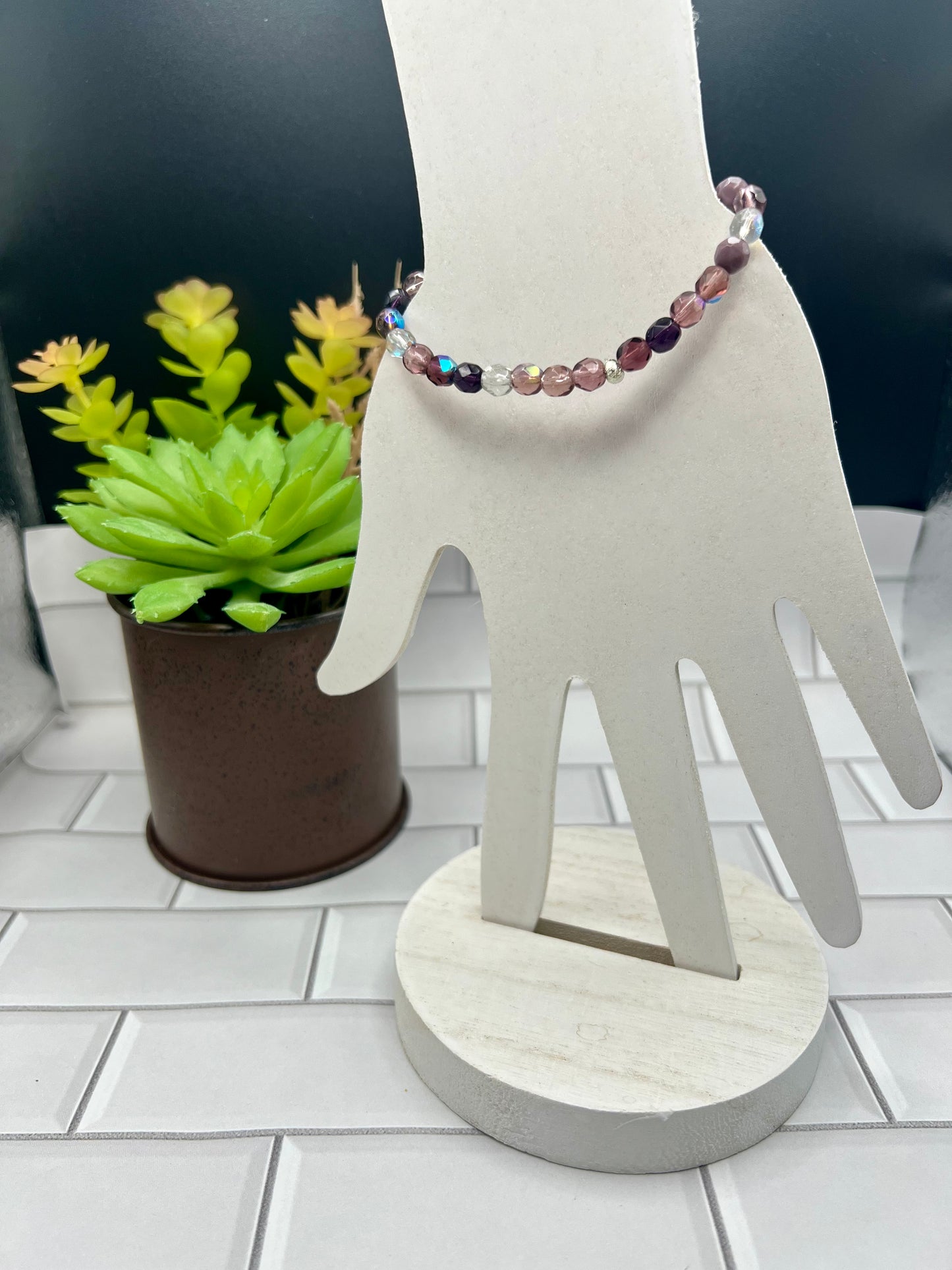 a white sculpture of a hand holding a beaded bracelet