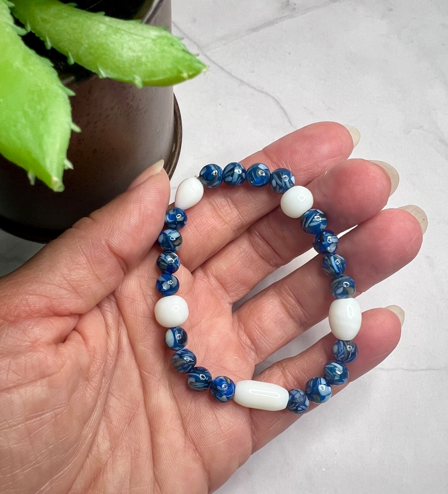 a woman's hand holding a blue and white beaded bracelet