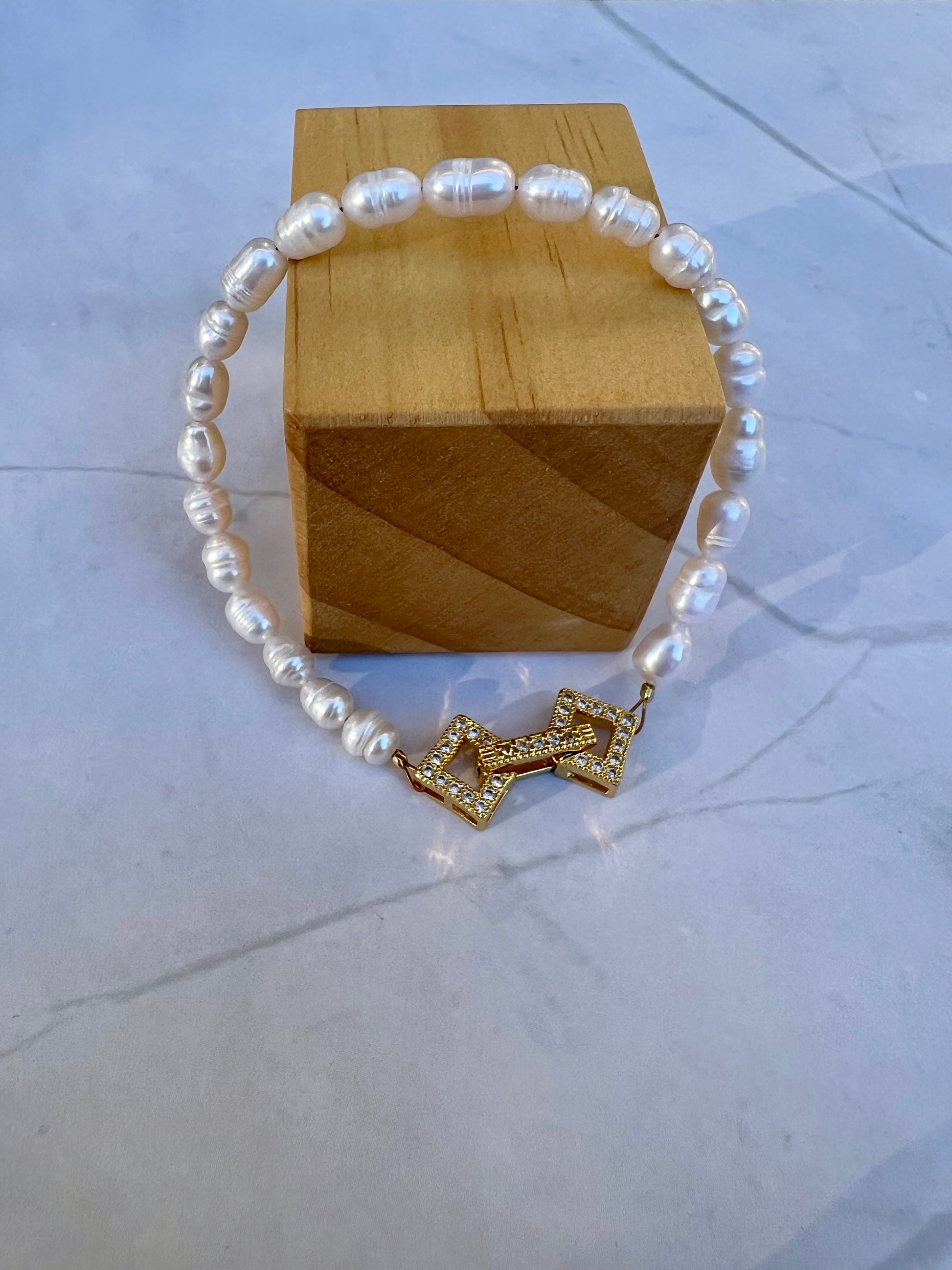 a white pearl bracelet with a gold cross charm