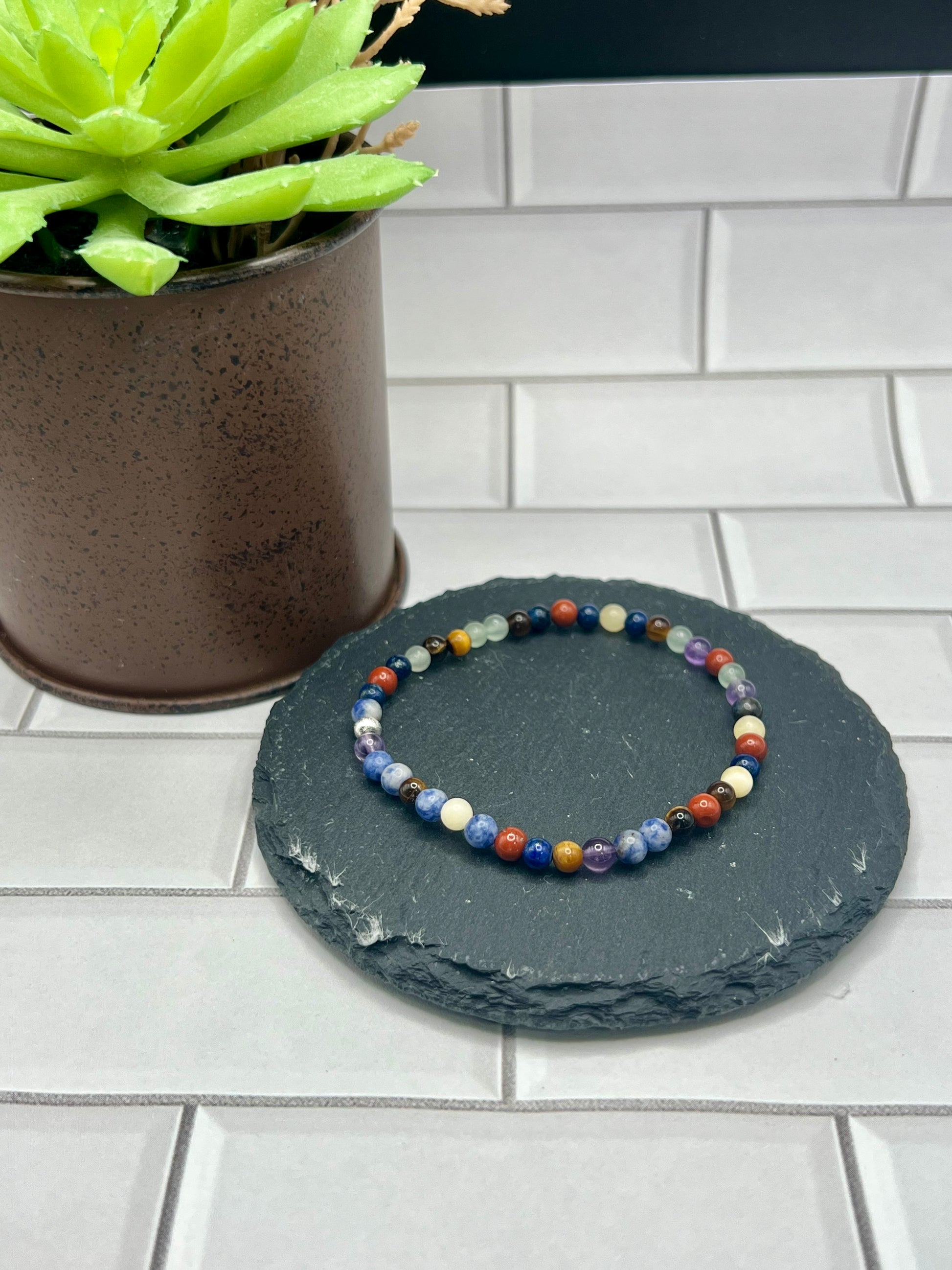 a stone with a beaded bracelet sitting next to a potted plant