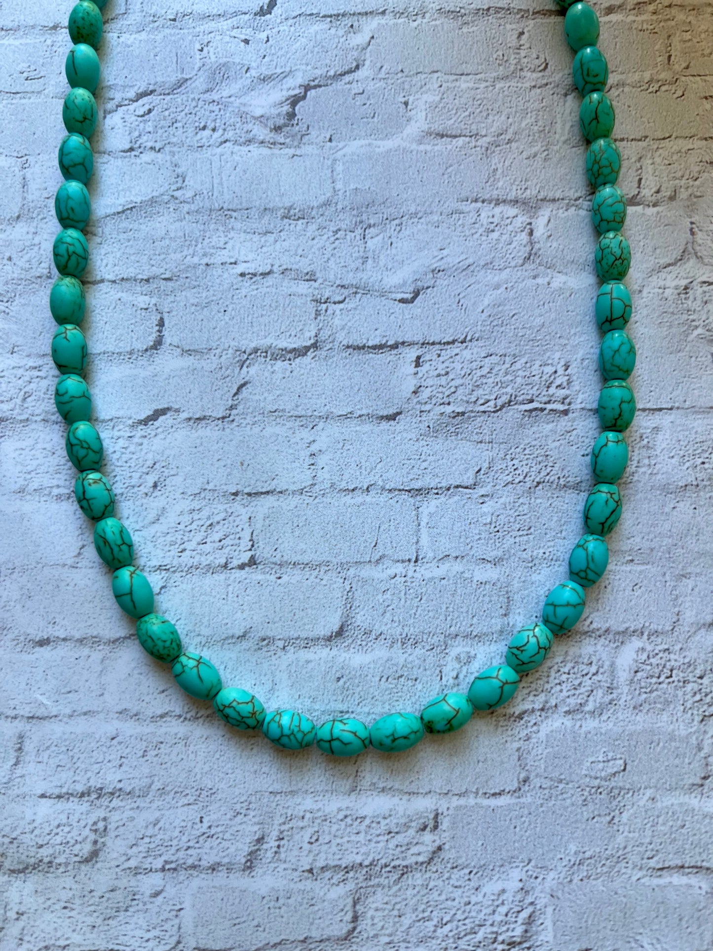 a necklace made of turquoise beads on a white brick wall