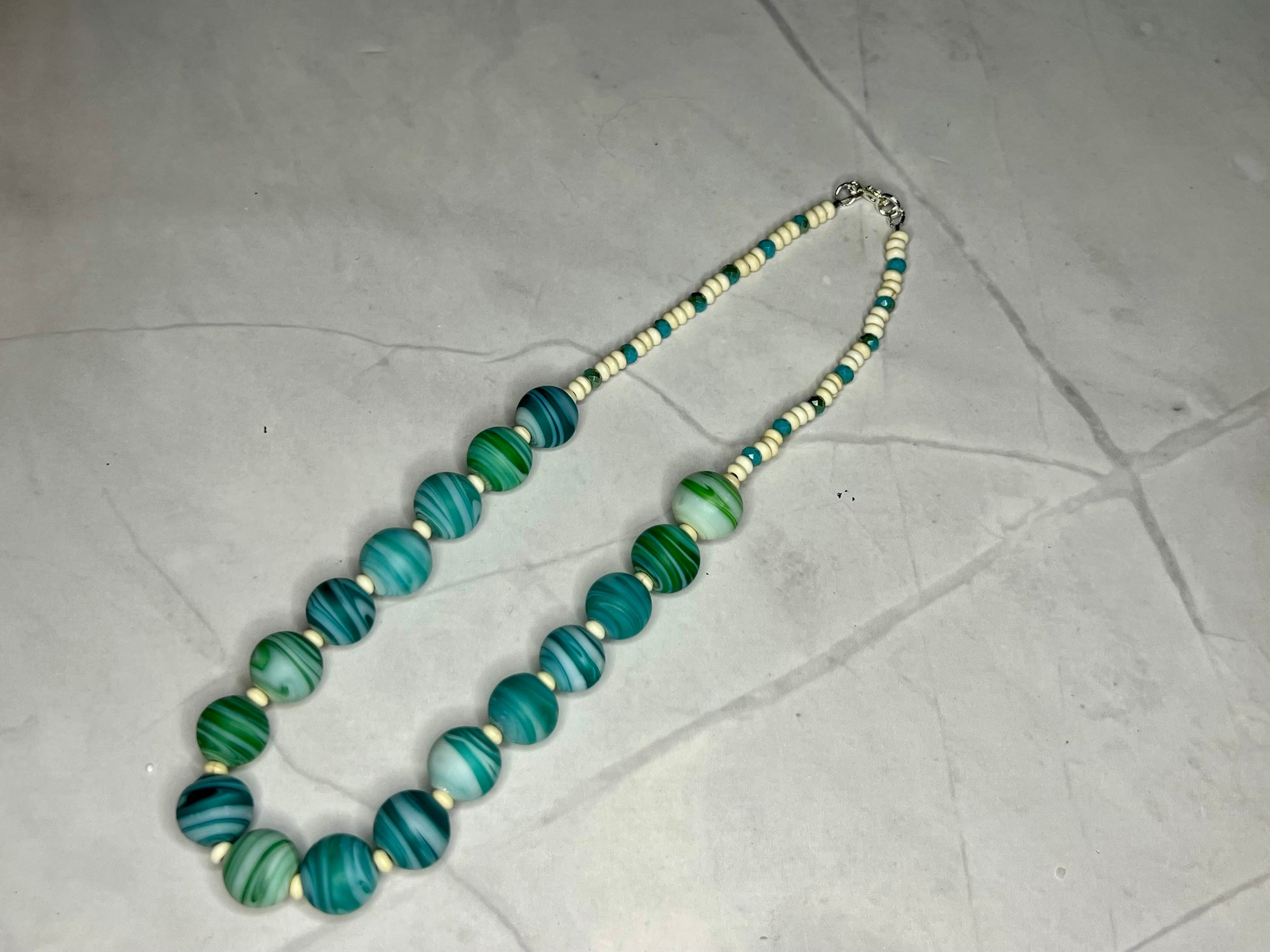 a necklace with green and white beads on a white surface