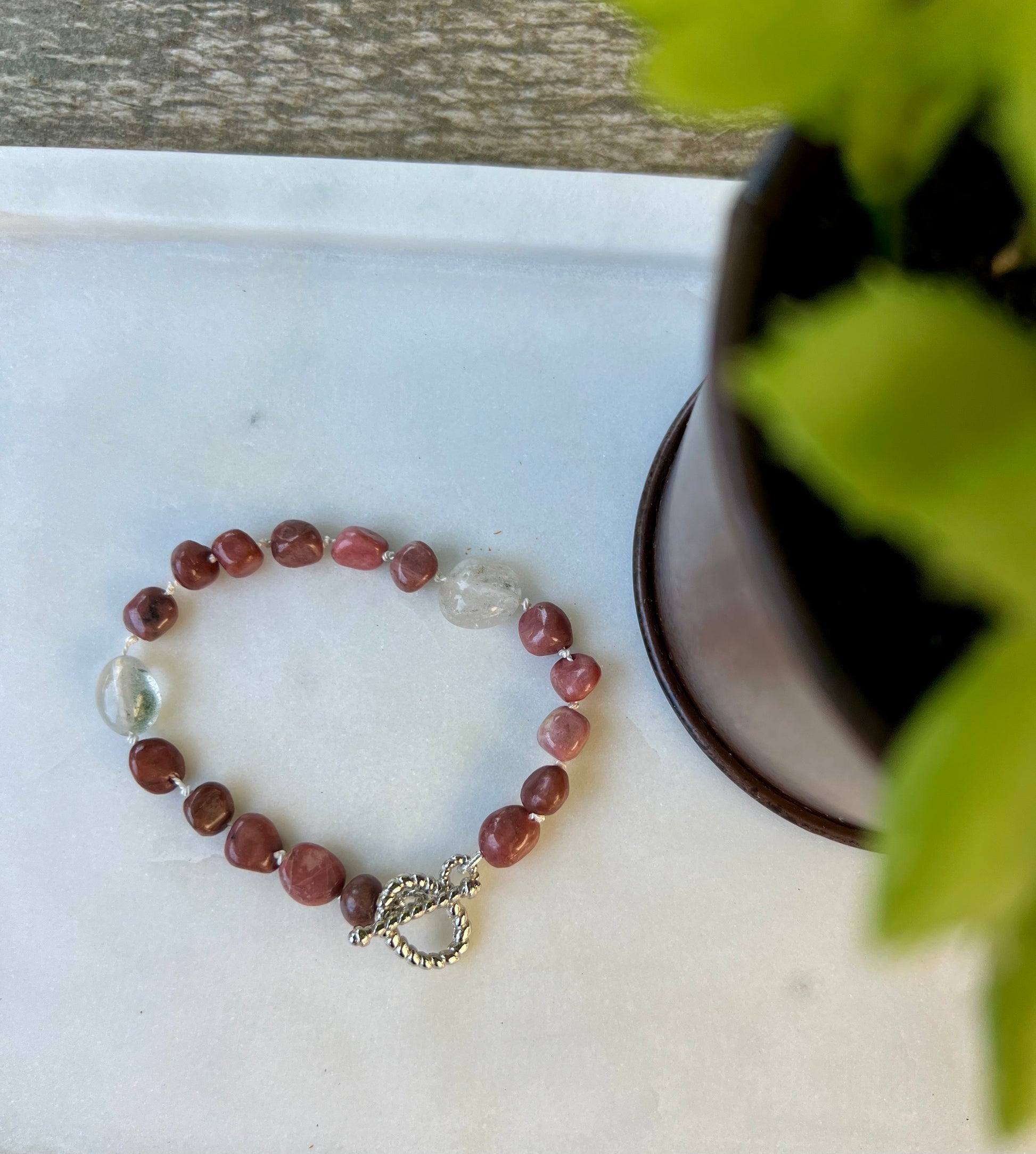 a beaded bracelet sitting on top of a table next to a potted plant