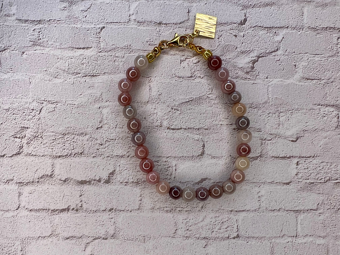 a bracelet with a gold charm on a brick wall