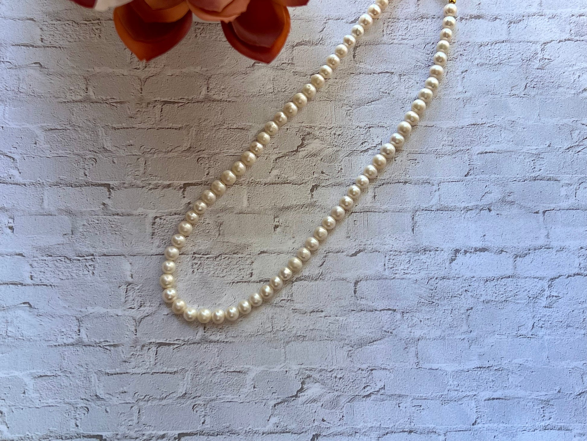 a white pearl beaded necklace on a white brick wall