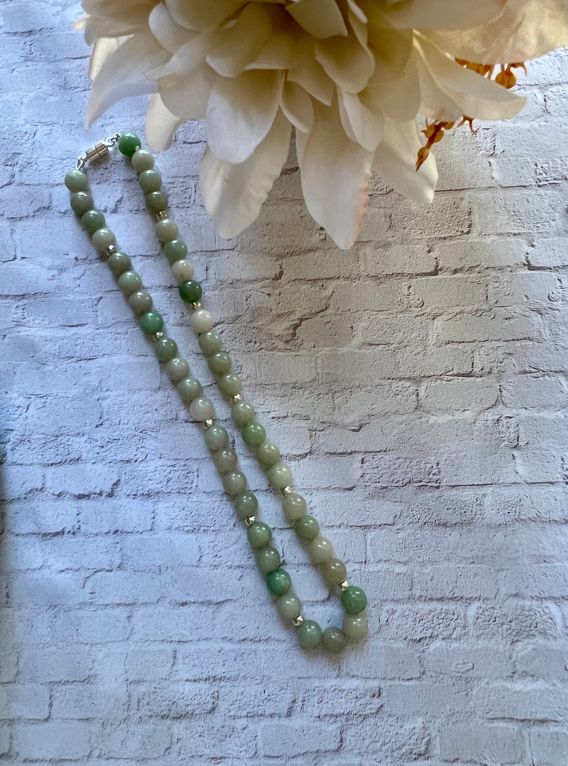 a white flower sitting next to a green beaded necklace