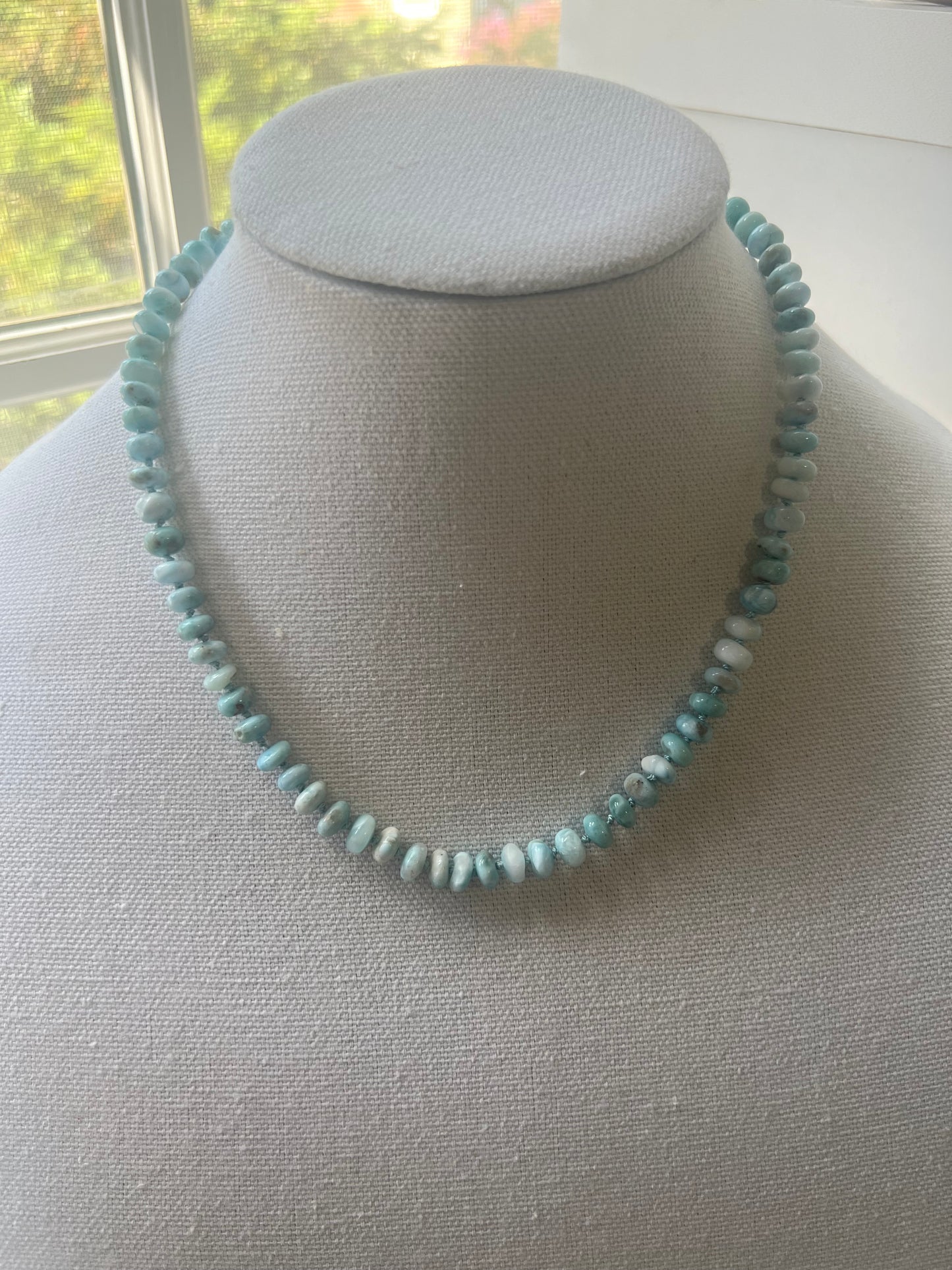 a blue beaded necklace sitting on top of a white pillow