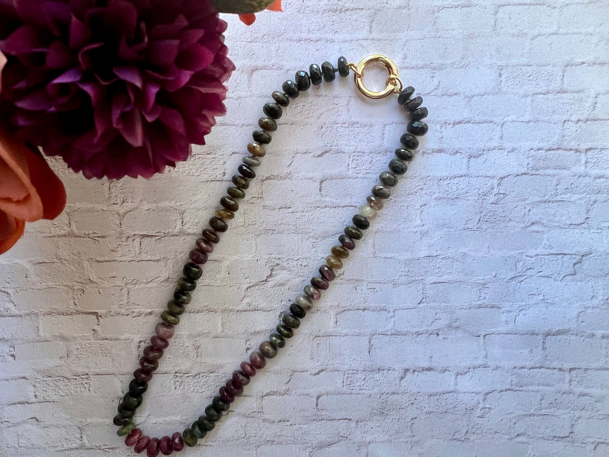 a long beaded necklace on a white brick wall