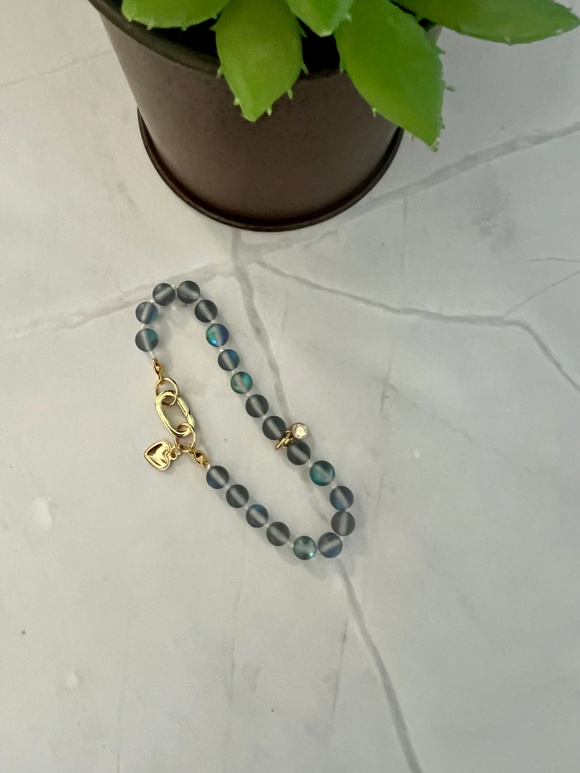 a beaded bracelet with a cross on it next to a potted plant