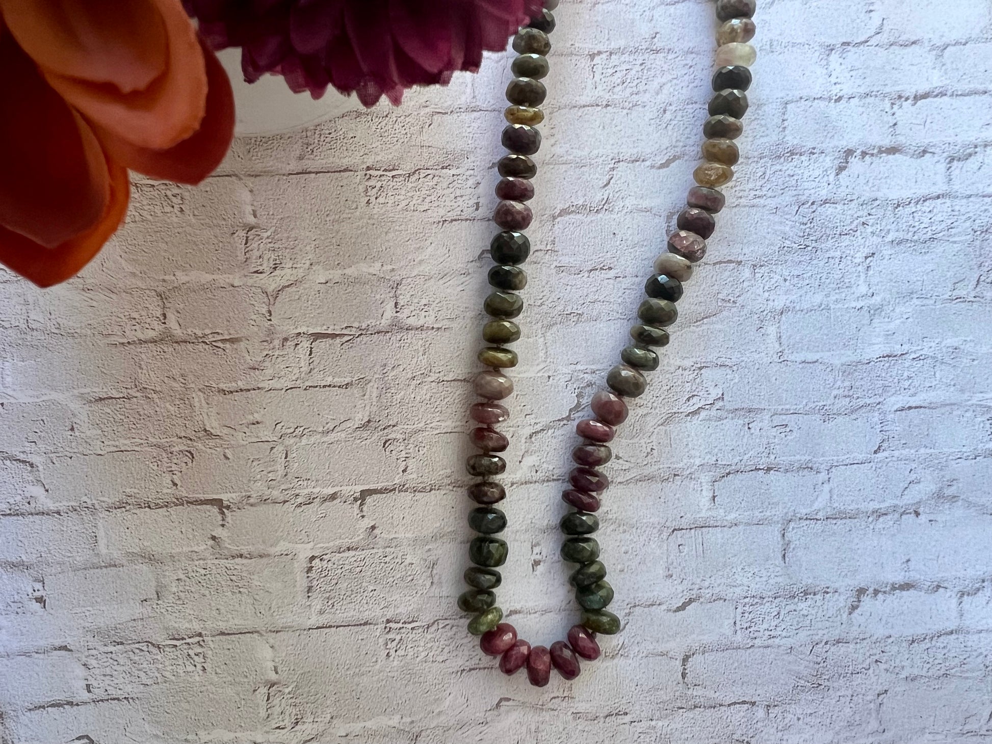 a long beaded necklace on a white brick wall