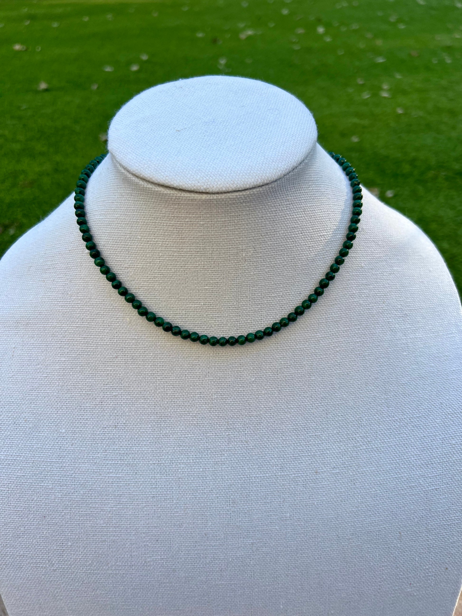 a white mannequin with a green beaded necklace on it