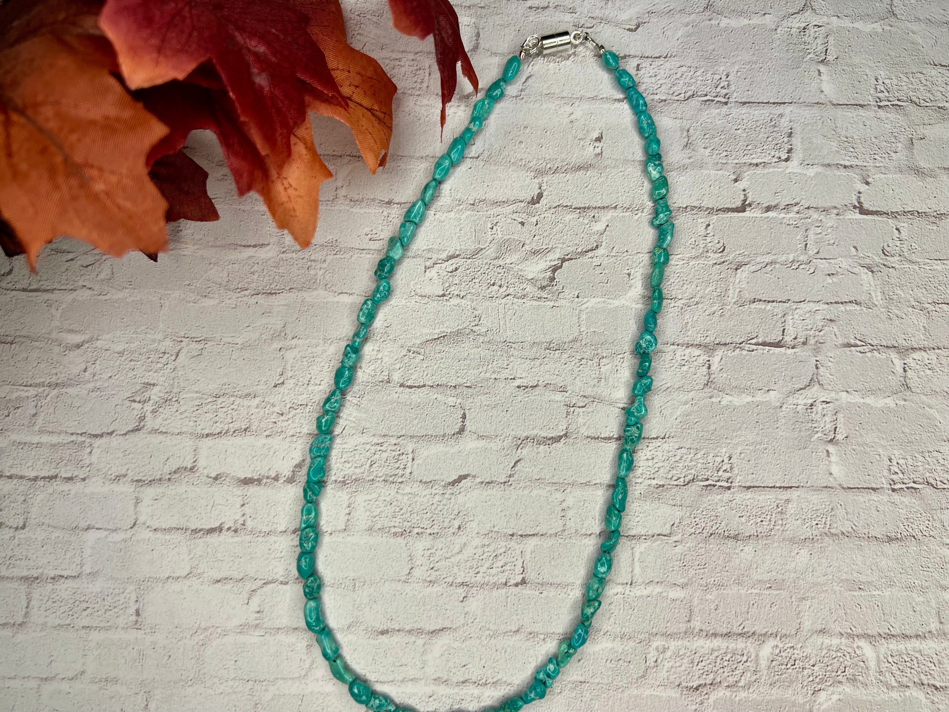 a green beaded necklace on a white brick wall