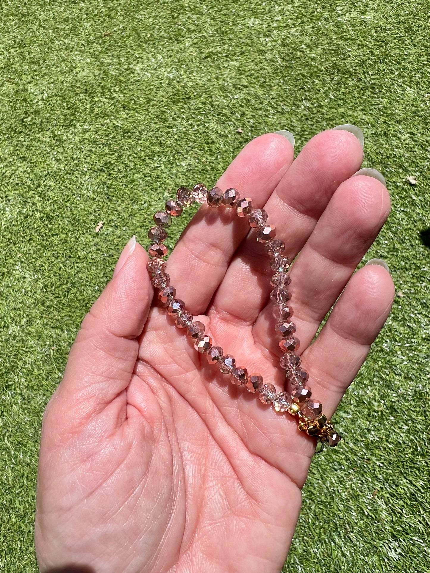 a hand holding a beaded bracelet on top of a green field