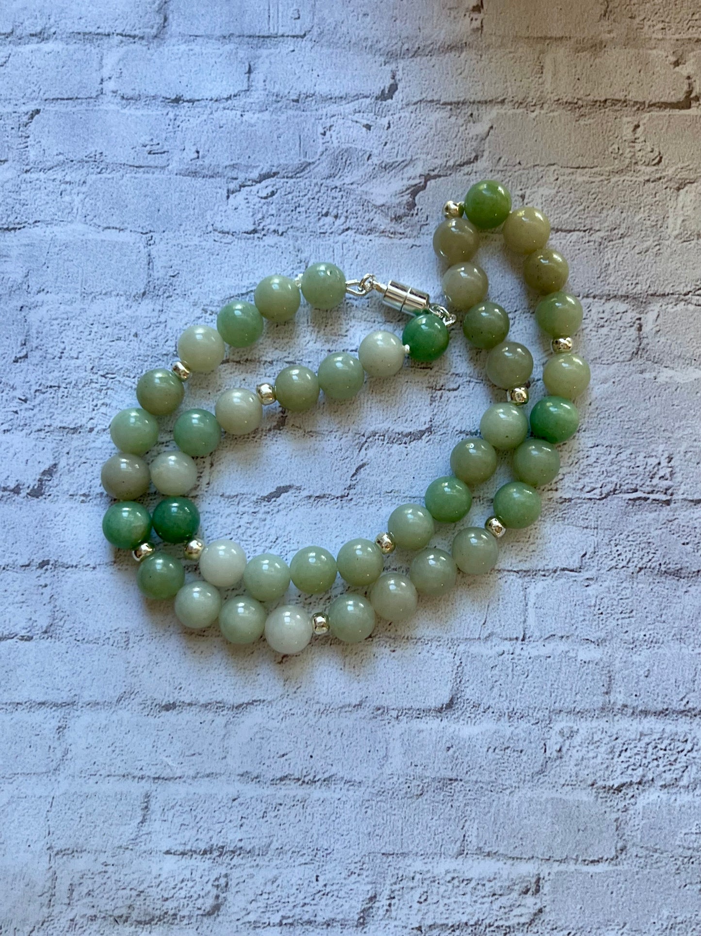 a green beaded necklace on a white brick wall