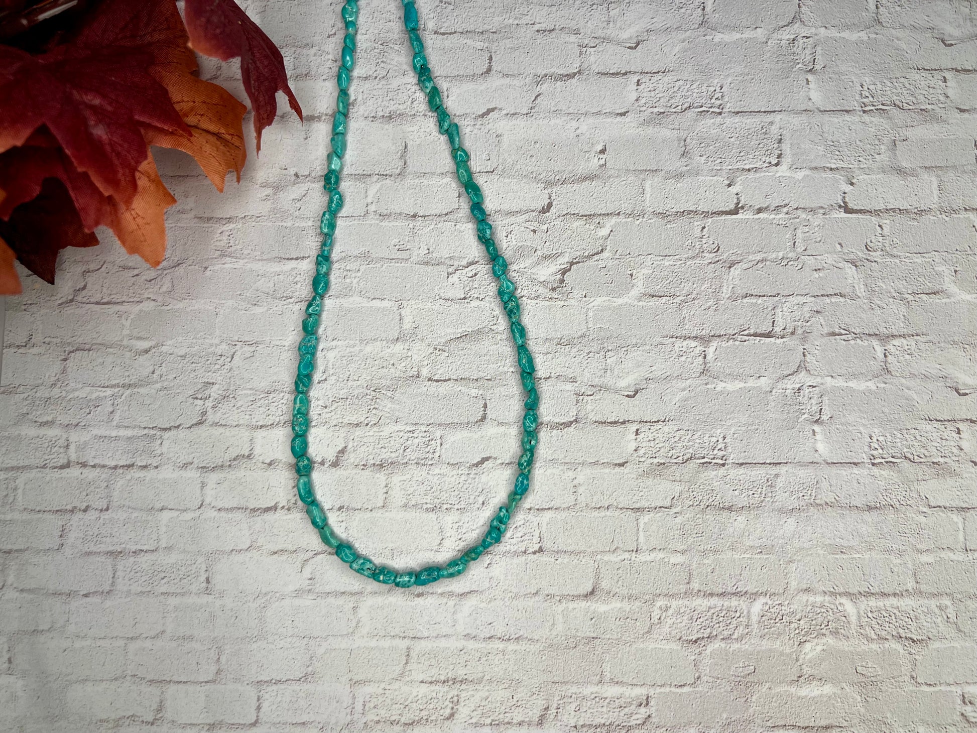 a green beaded necklace hangs on a brick wall