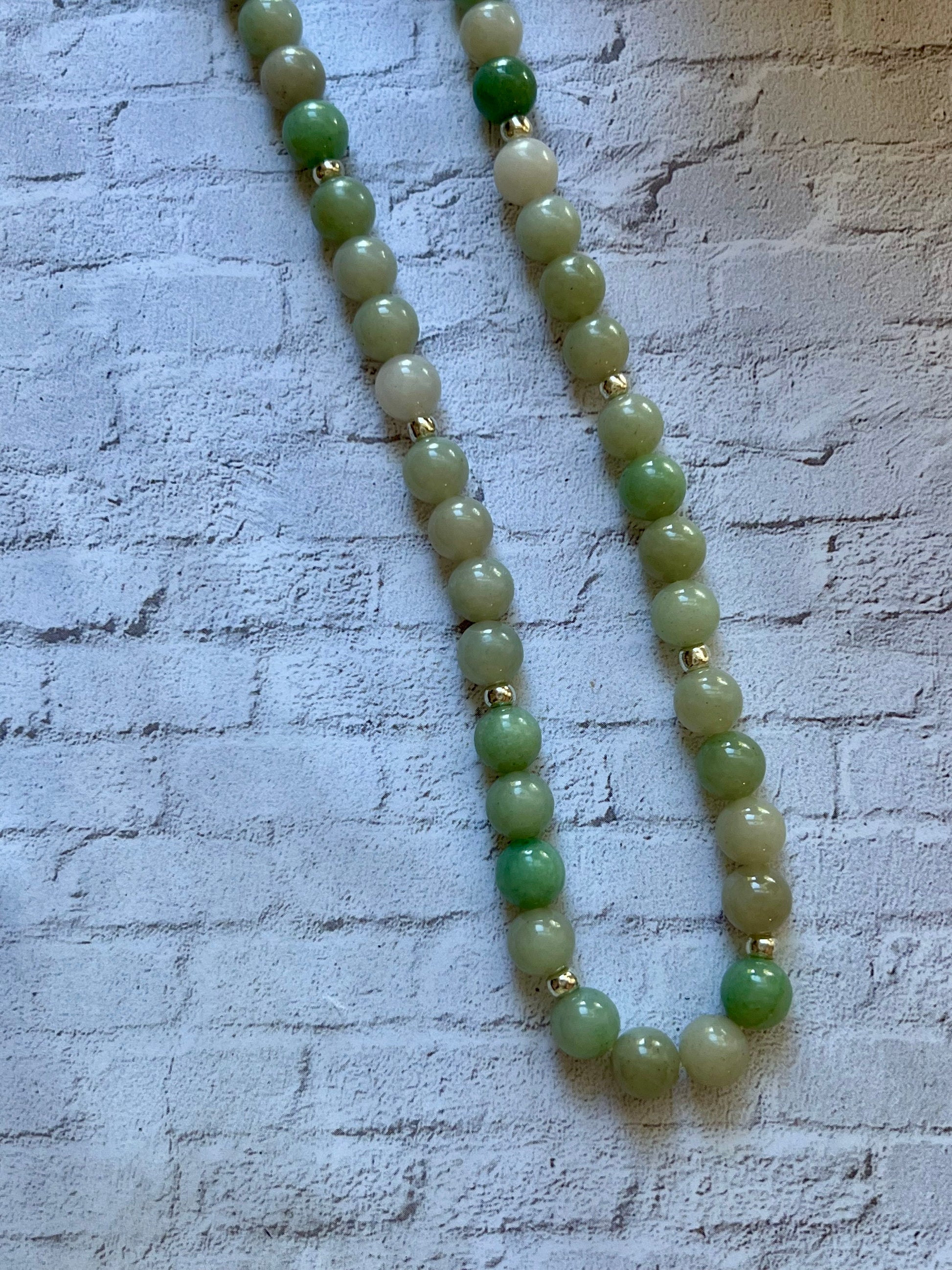 a green beaded necklace on a white brick wall