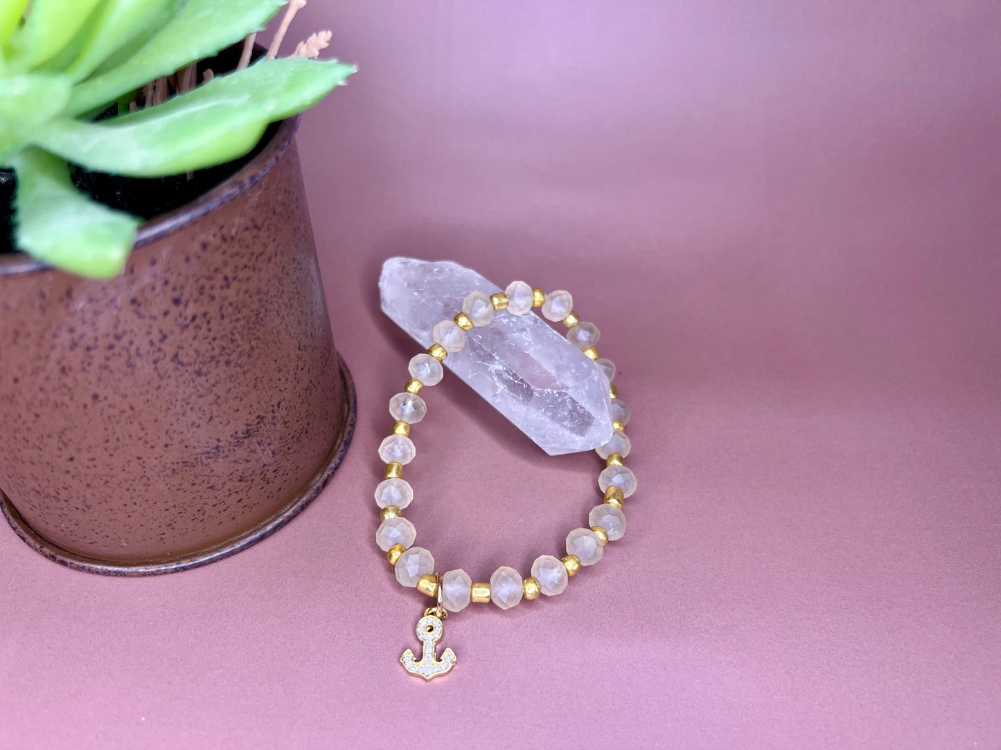 a beaded bracelet with a cross on it next to a potted plant