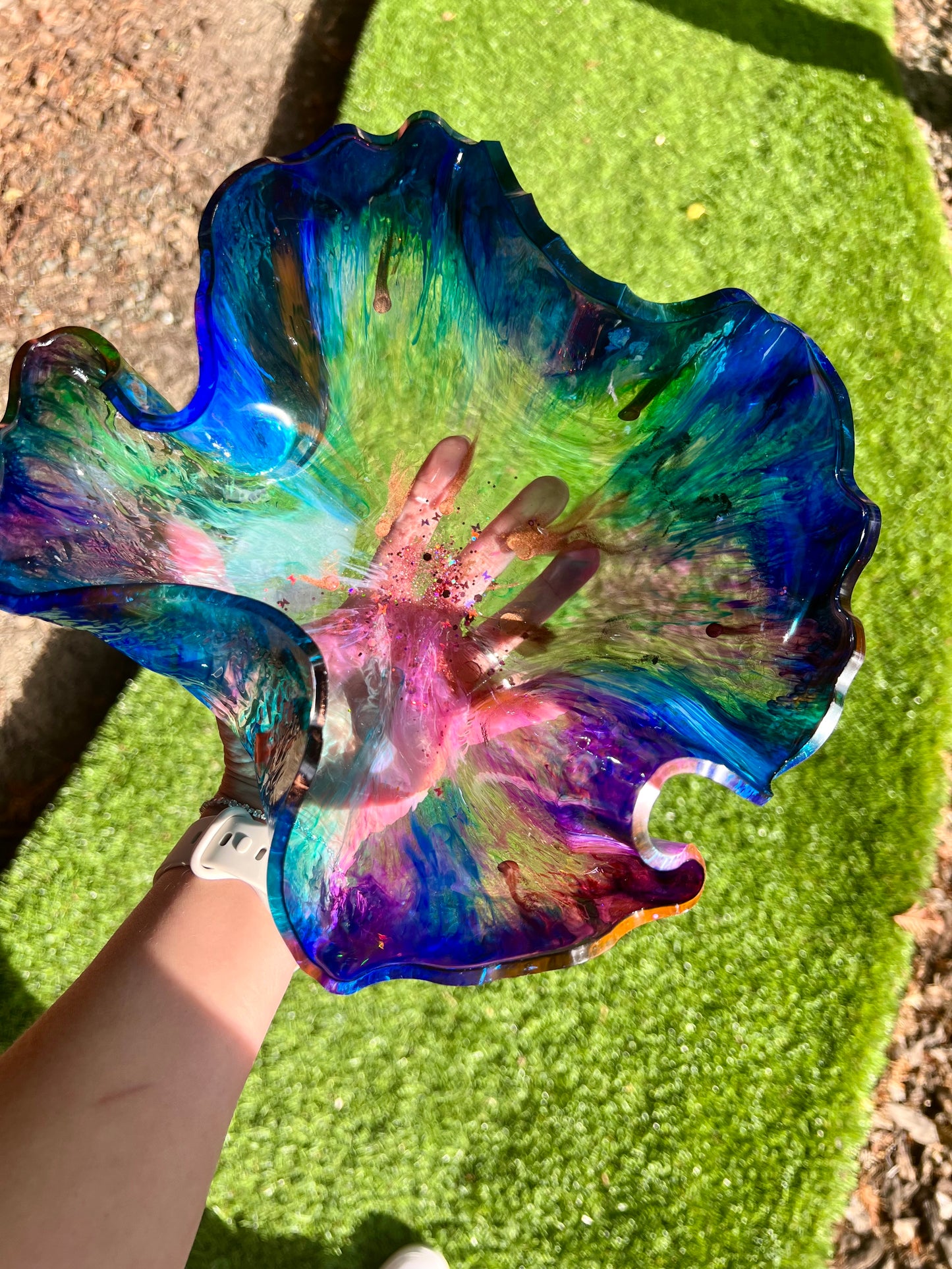 a hand holding a colorful flower shaped glass bowl