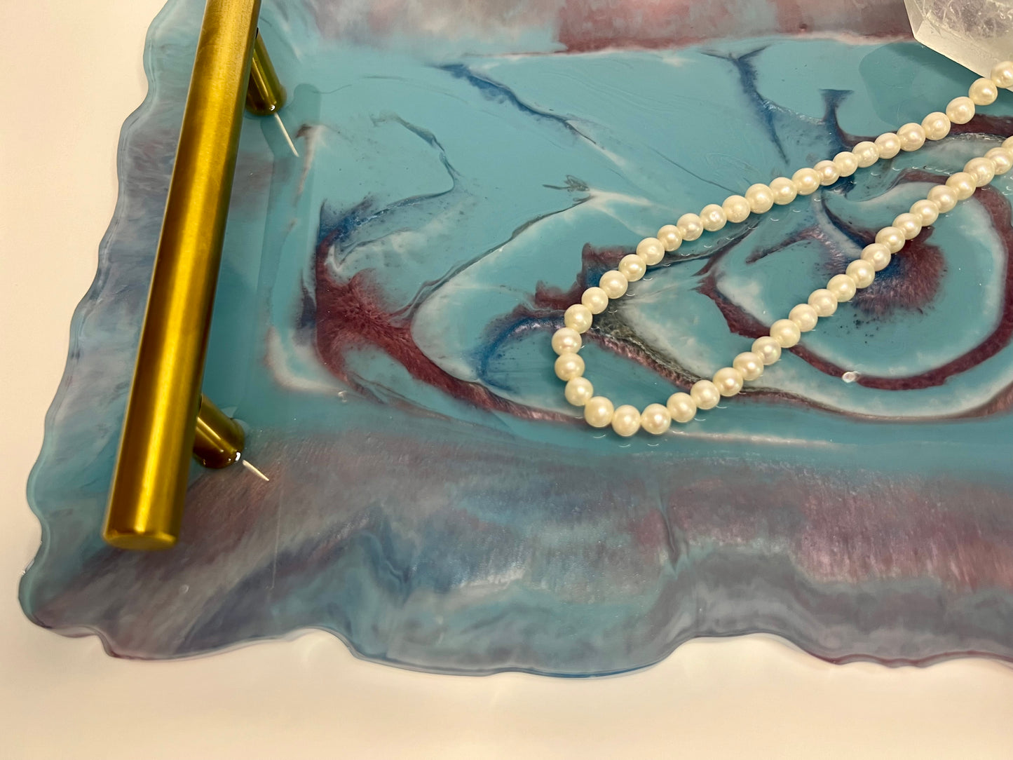 a pearl necklace on a blue plate with a gold pen