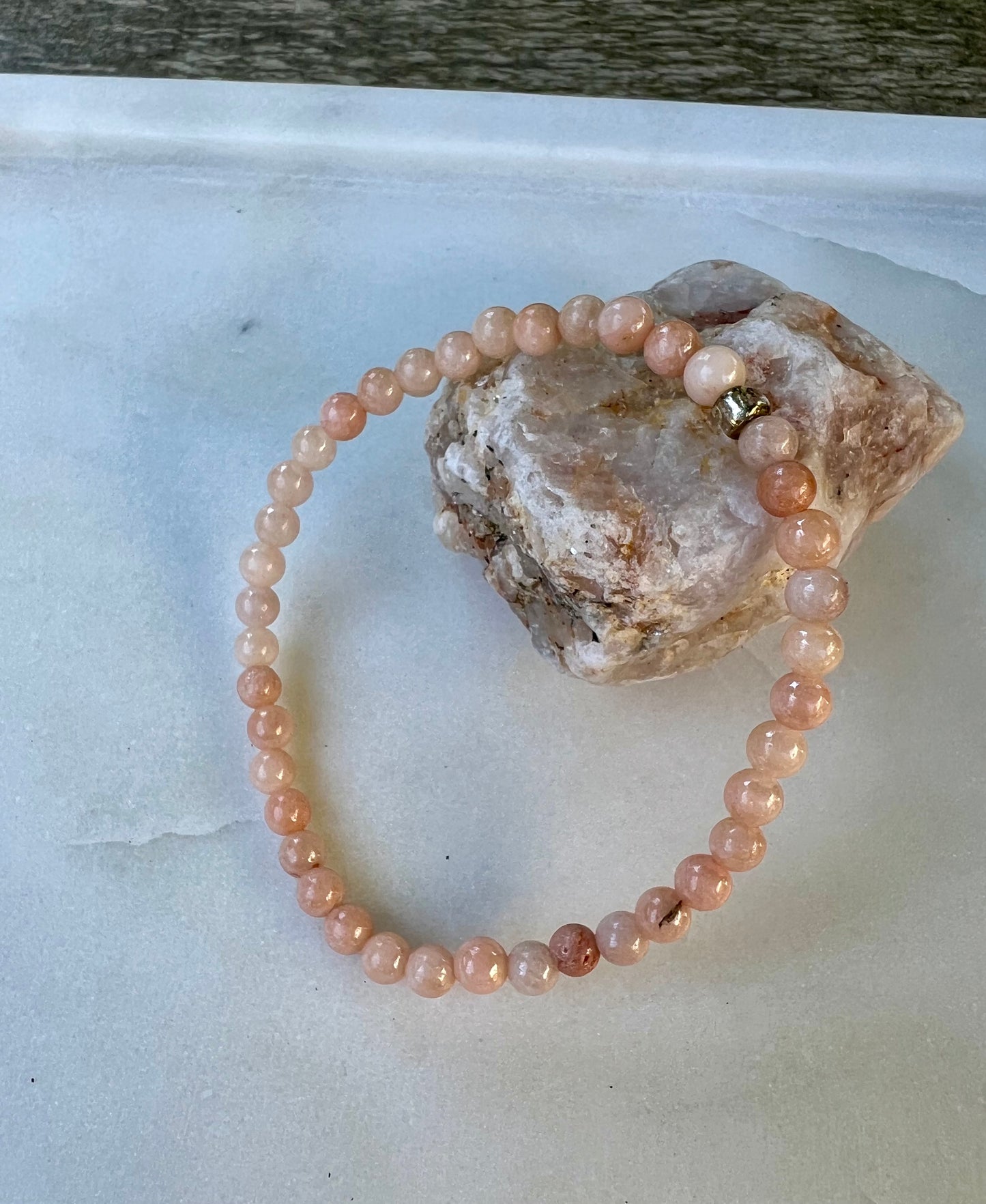 a pink beaded bracelet on top of a rock