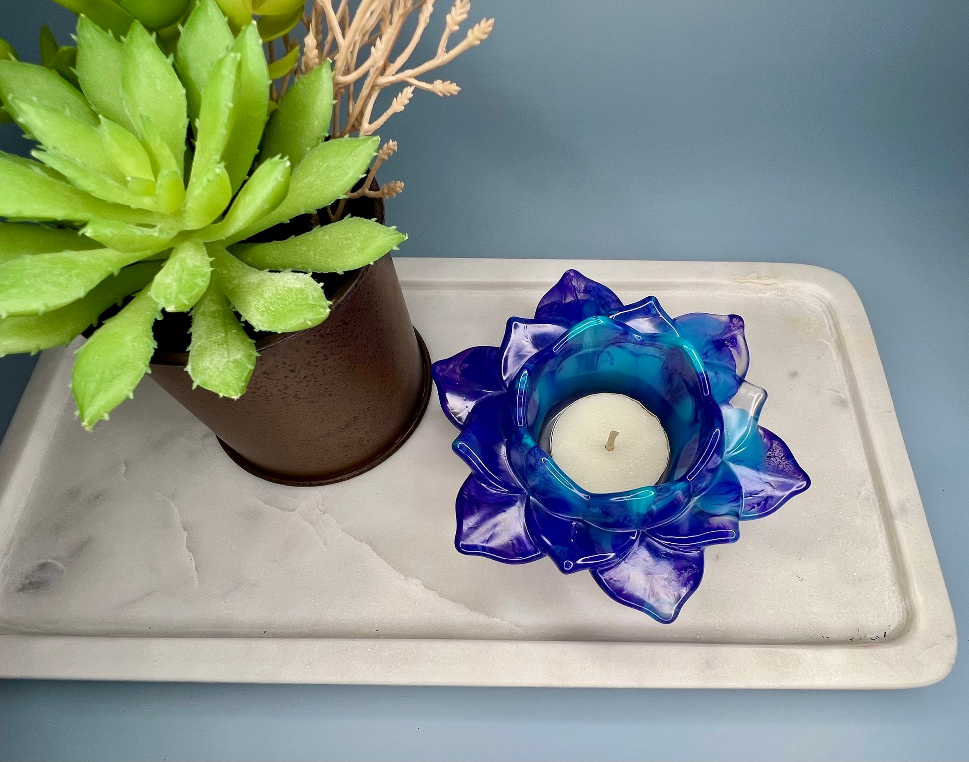 a blue flower candle holder next to a potted plant