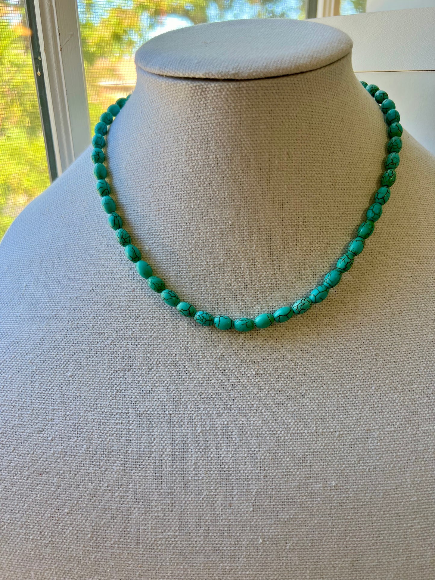 a necklace on a mannequin with a green bead