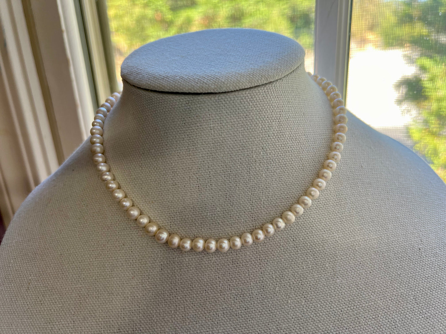 a white necklace on a mannequin in front of a window