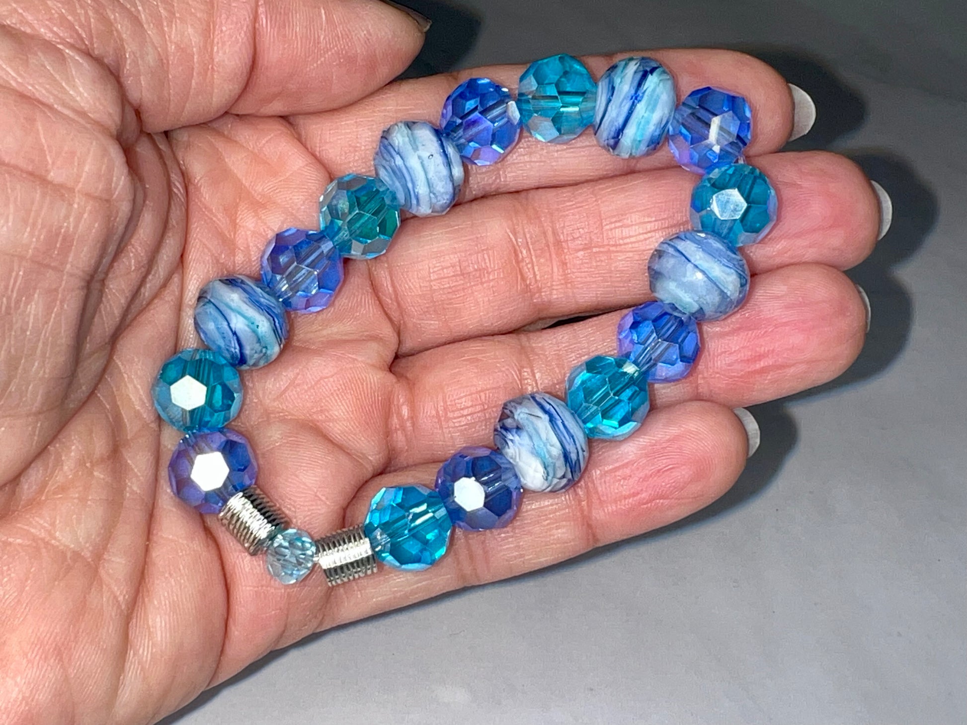 a hand holding a blue and white beaded bracelet