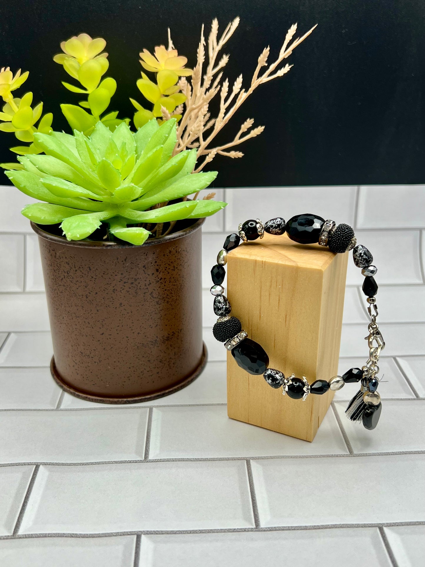 a wooden block with a black beaded bracelet next to a potted plant