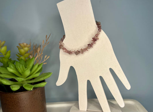 a hand with a beaded bracelet next to a potted plant