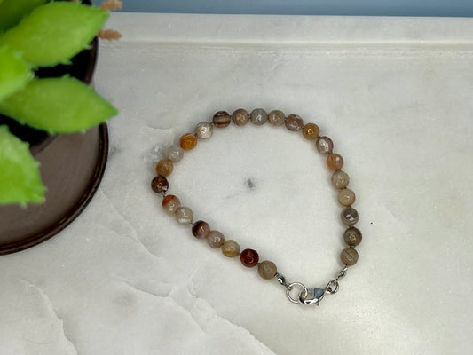 a beaded bracelet with a heart charm sits on a table next to a pot