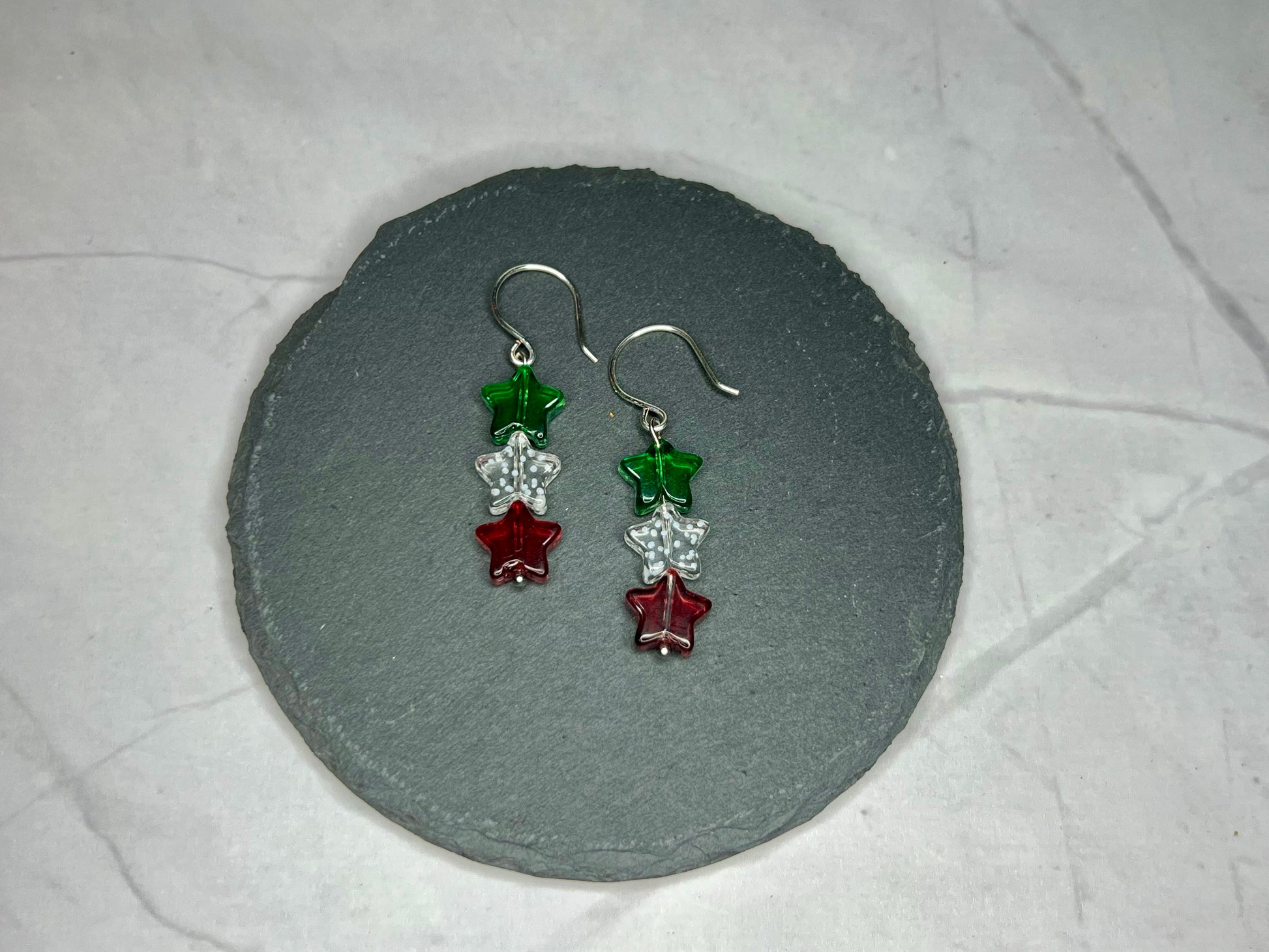 a pair of red and green earrings sitting on top of a stone