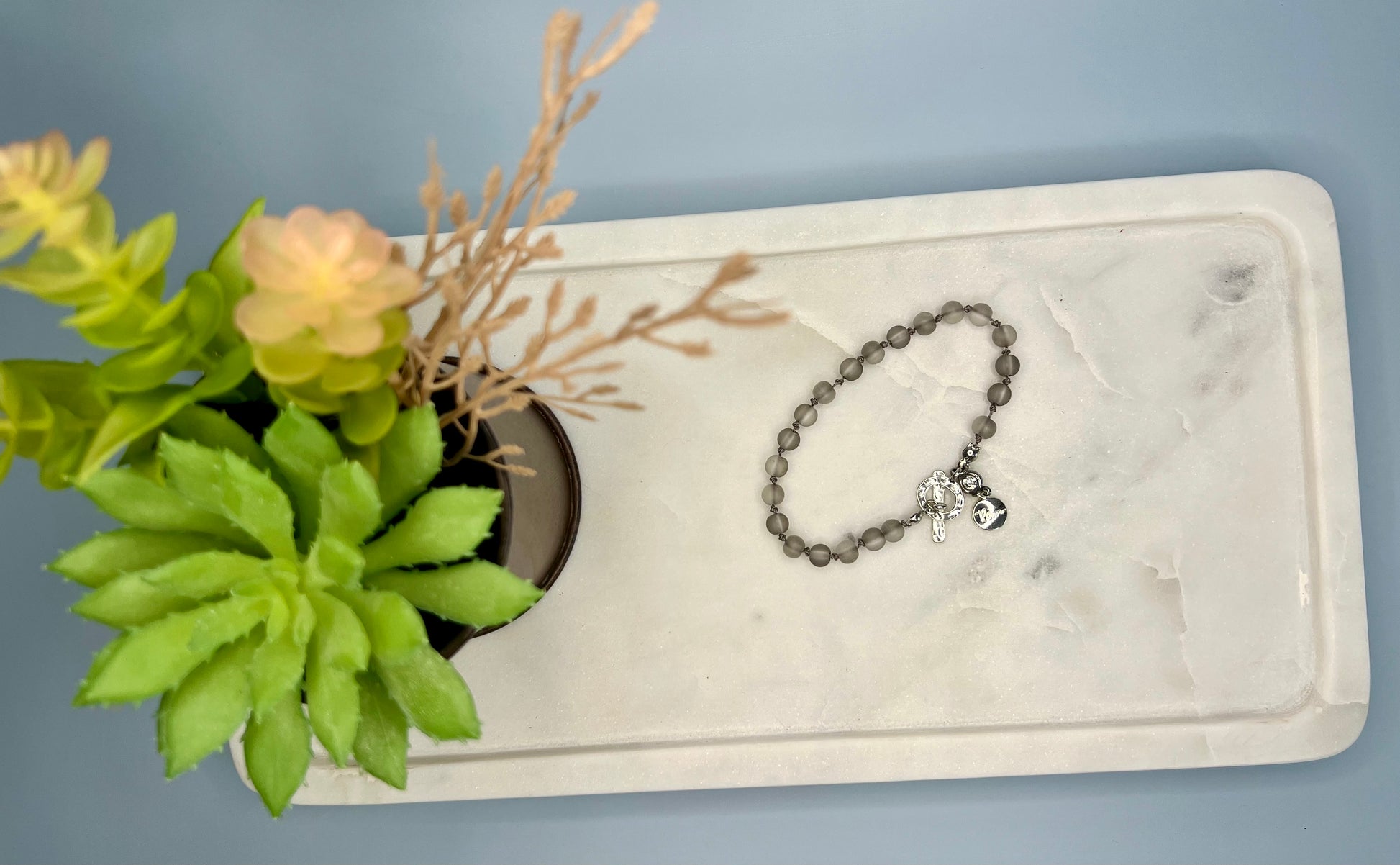 a white marble tray with a chain bracelet and a potted plant