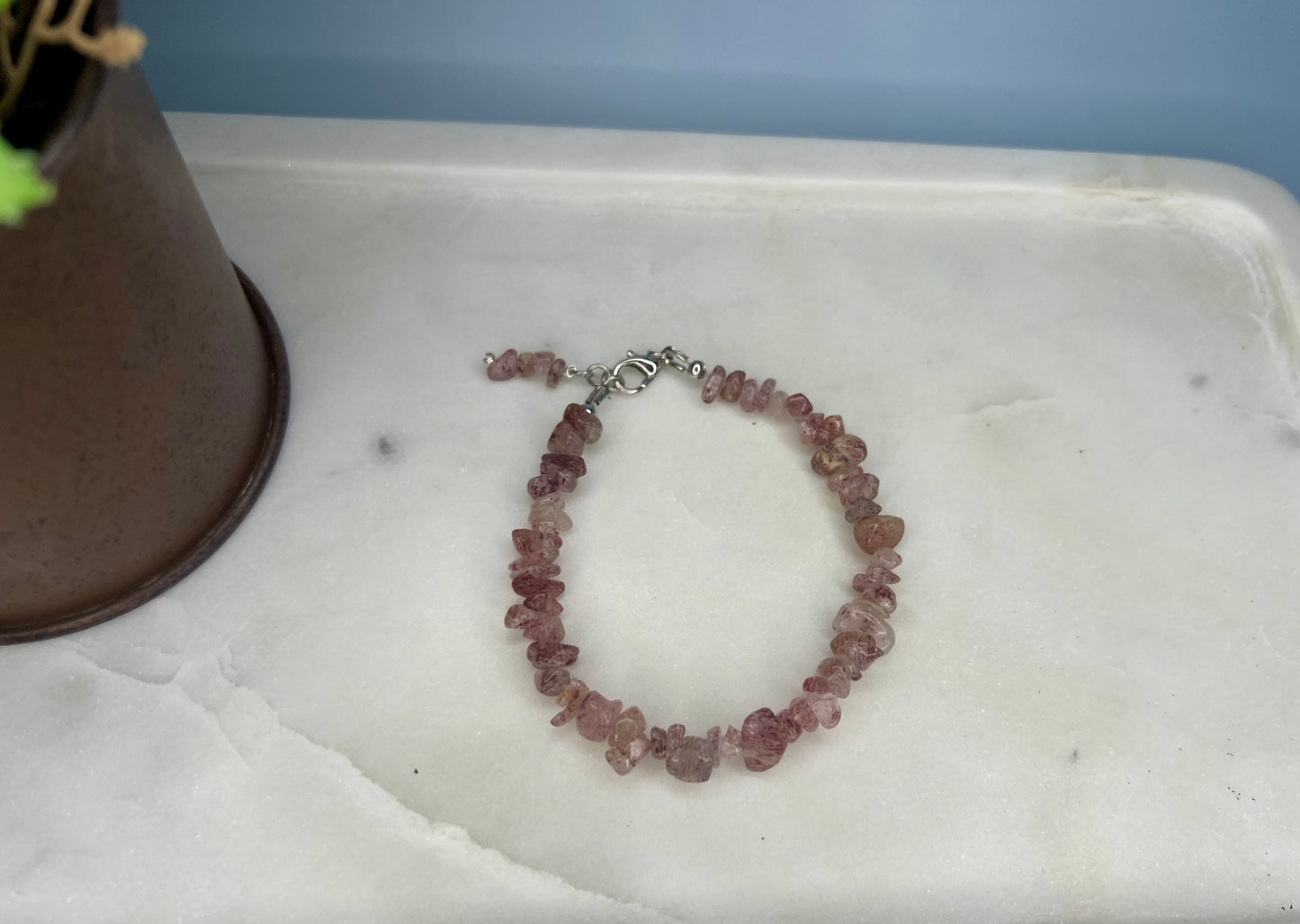 a pink beaded bracelet on a tray next to a potted plant