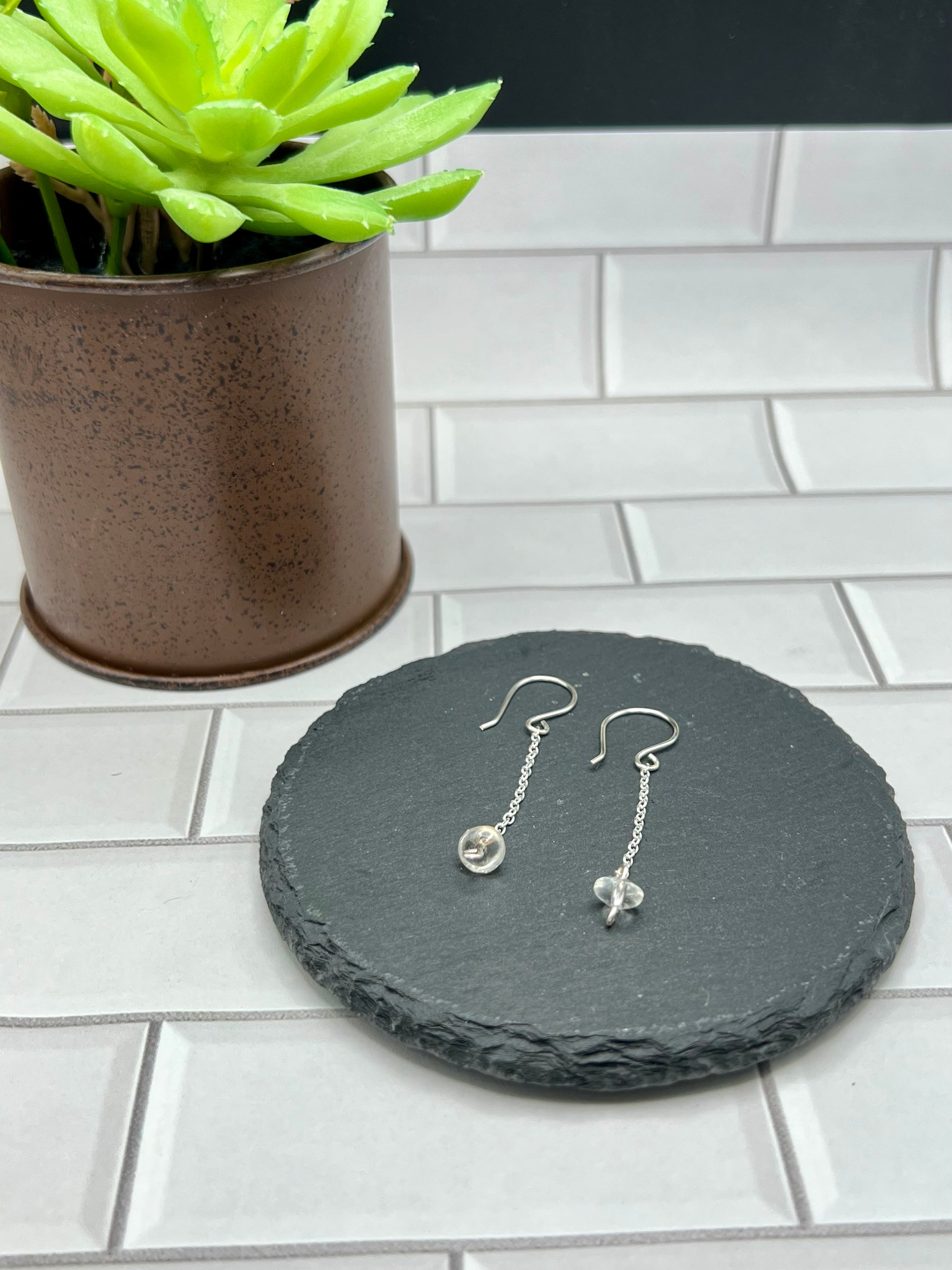 a pair of earrings sitting on top of a tile floor next to a potted