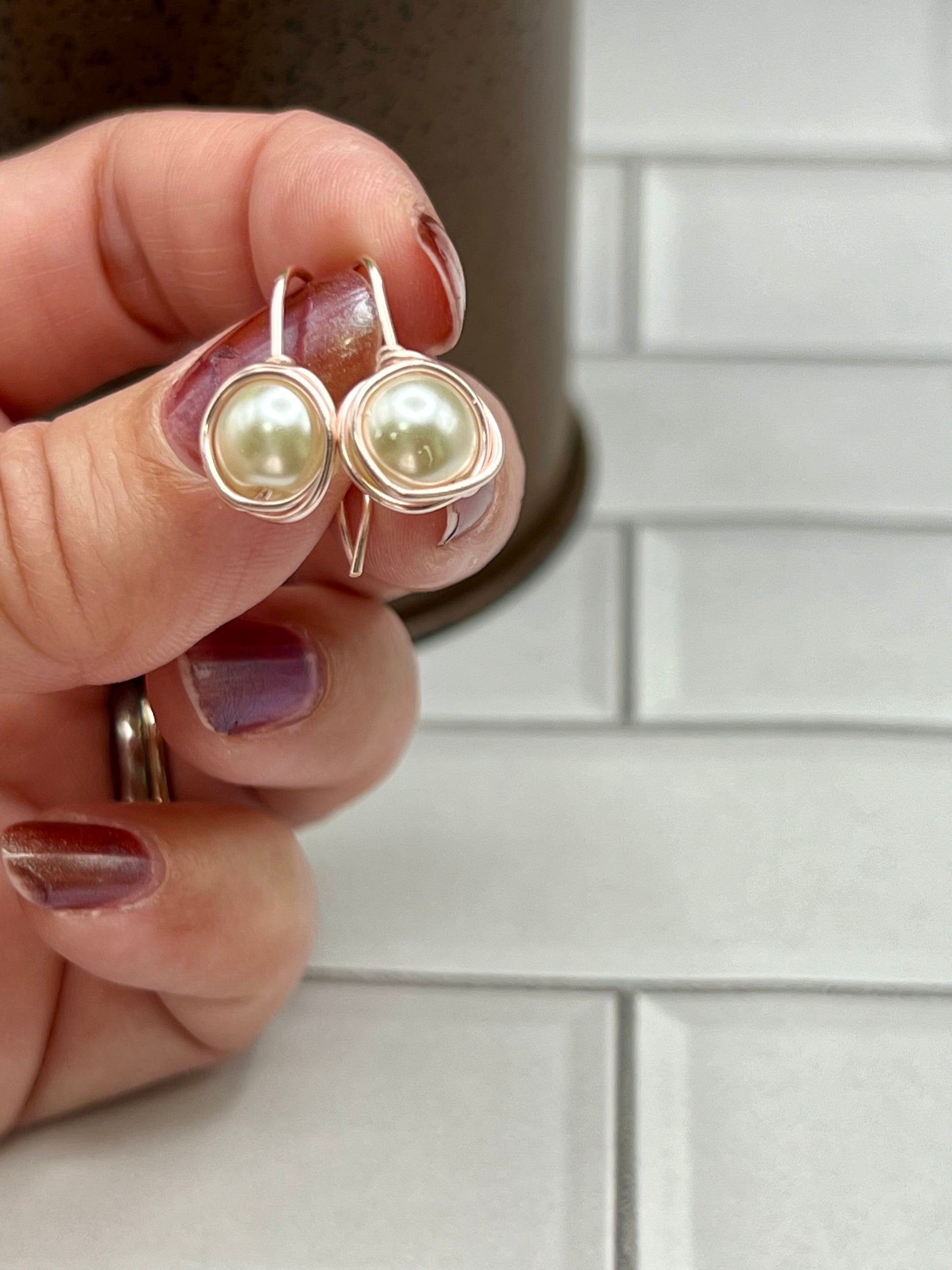 a woman's hand holding a pair of pearl earrings